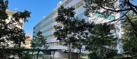 A multi-story building with balconies, surrounded by greenery and trees.