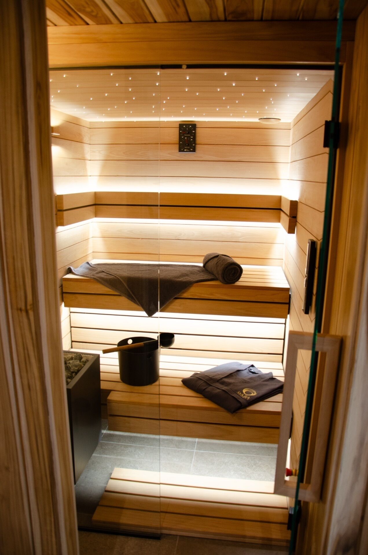 A sauna room with wooden slats, a towel, a bucket, and a small heater.