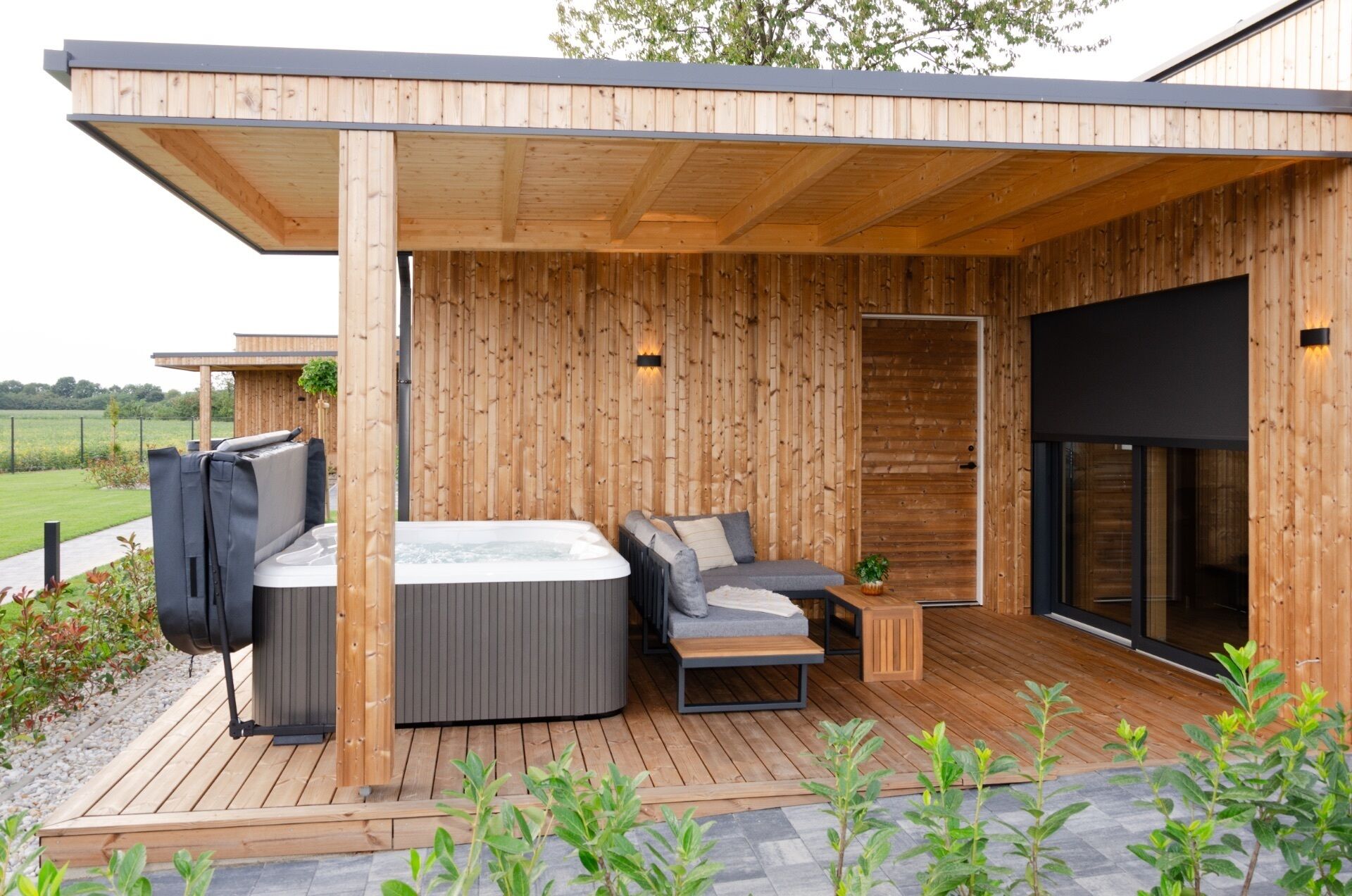 A modern outdoor hot tub area with a wooden deck, a sofa, and a table.