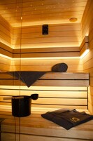 Una sauna con bancos de madera, un recipiente negro y una toalla.