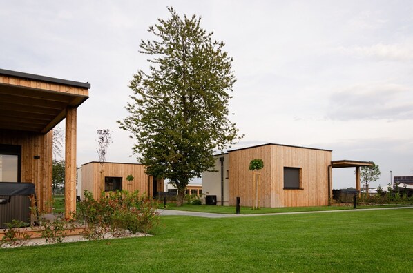 A modern building with a wooden facade, a large tree in the center, and a well-maintained lawn. - Oaza Luxury Resort (Moravske Toplice)