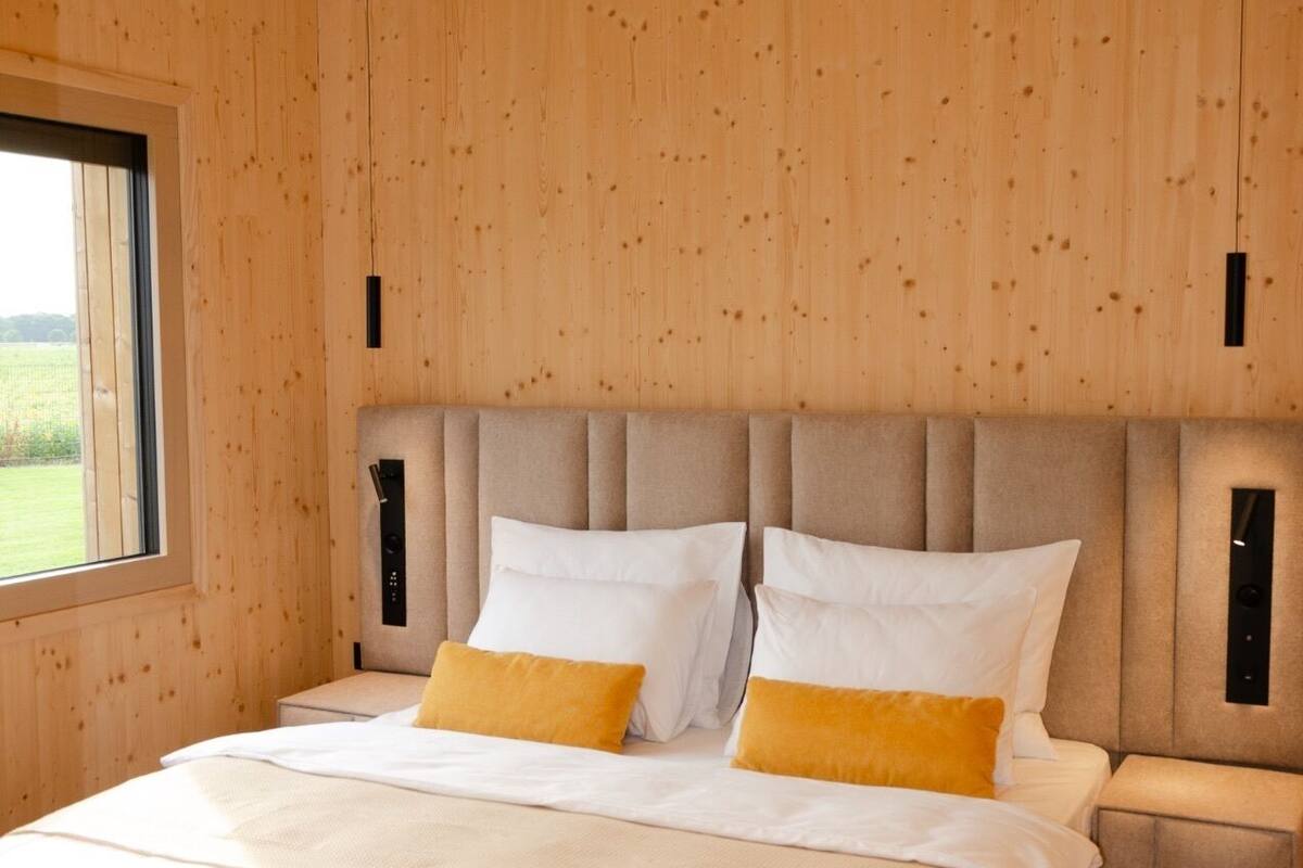 Un dormitorio con pared de madera, una cama grande con ropa de cama blanca y amarilla, y una ventana que ofrece vistas al exterior.