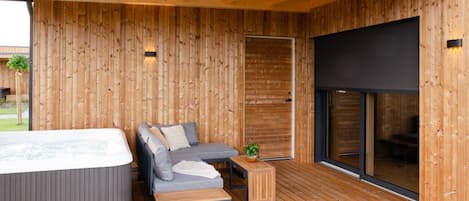 Una terraza de madera con un jacuzzi, un sofá y una pequeña mesa.