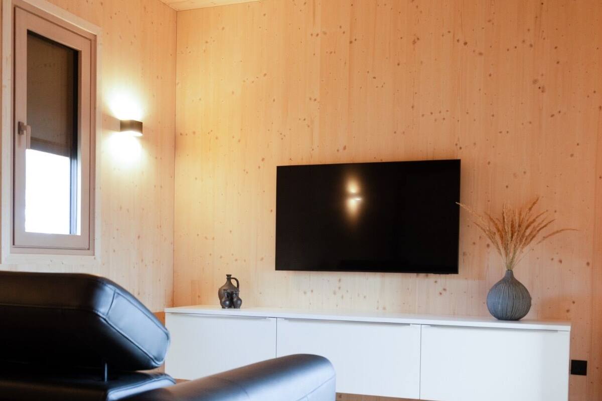 Una sala de estar moderna con un sofá de cuero negro, un mueble de entretenimiento blanco y un televisor de pantalla plana montado en una pared de madera.