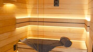 A sauna with wooden walls, a bench, a towel, a bucket, and a heater.