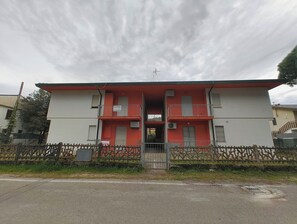 A two-story building with balconies, a gated entrance, and a red and white facade. - Welcoming apartment for five guests in Rosolina (Rosolina Mare)
