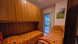 Una habitación con dos camas individuales, armarios de madera, una puerta que da a un espacio exterior y un cuadro en la pared.