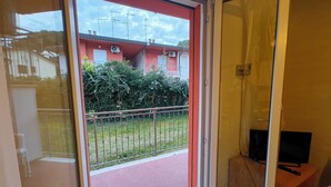 Una habitación con una puerta corrediza de vidrio que da a un balcón, un televisor sobre un soporte de madera y una mesita.