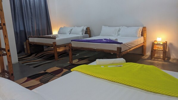 Ein Zimmer mit zwei Einzelbetten, einem großen Bett, einem kleinen Tisch mit Lampe und einem gemusterten Teppich.