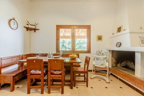 A dining area with wooden furniture, a fireplace, and a window with a view of greenery. - GuestHost - A welcoming and spacious 100-square-meter villa, perfect for seven people, featuring a private entrance and private outdoor parking for two vehicles.The property is located in Nuraxi Figus, a quiet hamlet of Gonnesa: from here, guests can vis (Nuraxi Figus)