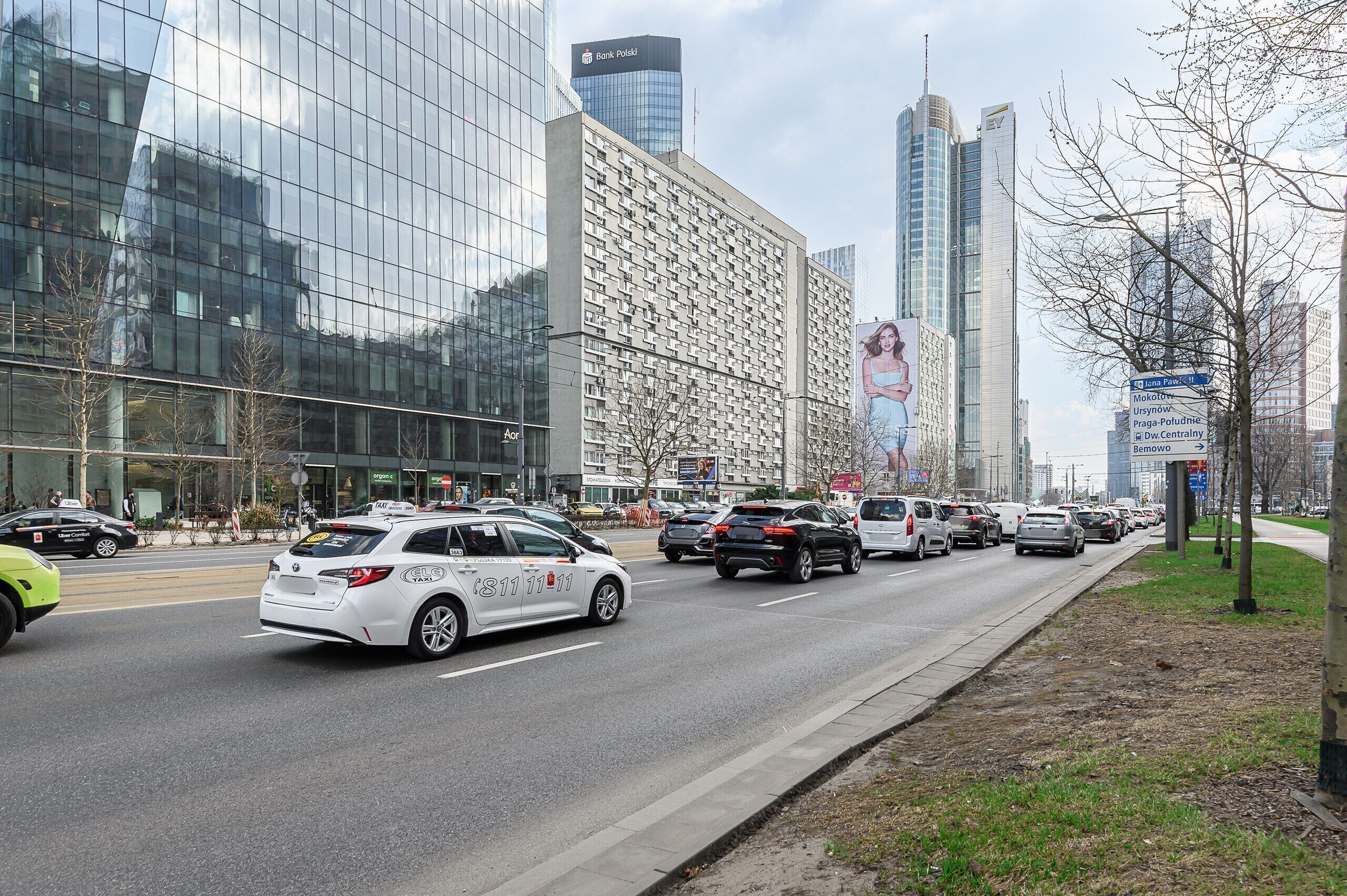 A city street with modern buildings, a taxi, and a pedestrian crossing.