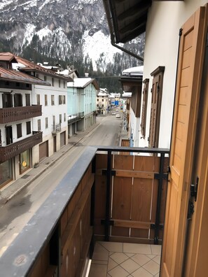 A balcony with a view of a mountain range, a wooden fence, and buildings with balconies.
