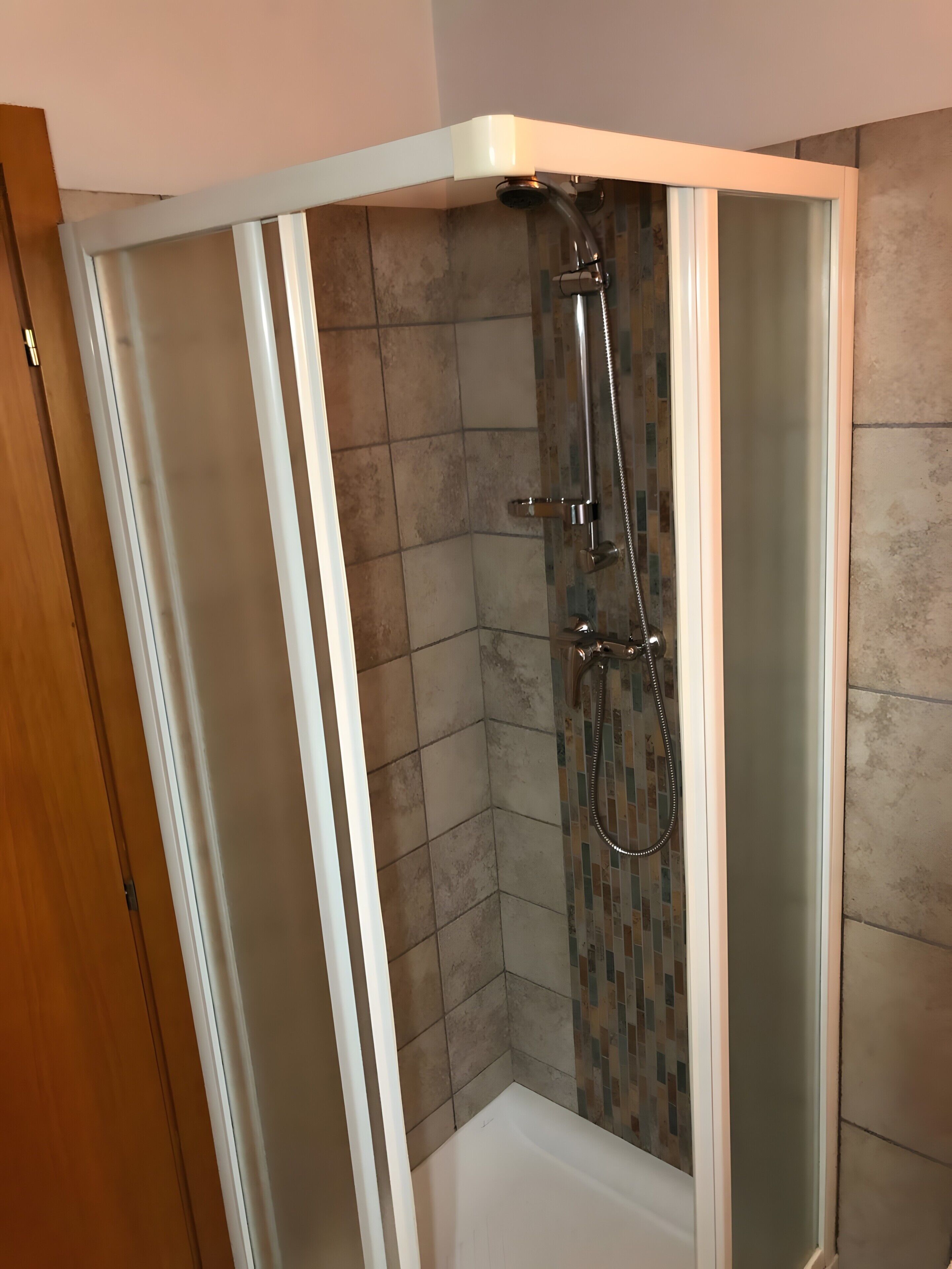 A corner shower with a glass door, tiled walls, and a showerhead.