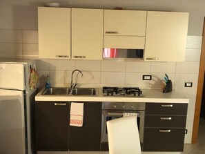 A kitchen with a refrigerator, stove, sink, and cabinets.