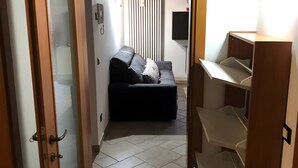 Ein Flur, der in einen Wohnbereich mit einer Couch, einem Heizkörper und einem Fernseher führt.