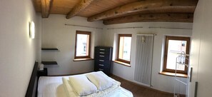 A bedroom with a bed, a dresser, a radiator, and two windows.