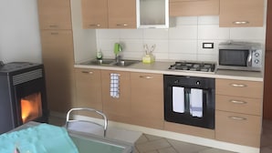 A modern kitchen with wooden cabinets, a gas stove, a microwave, and a built-in oven. - Apartment 'Nina' with Shared Terrace and Wi-Fi (Santo Stefano di Cadore)