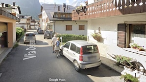 A narrow street with parked cars, a pedestrian, and buildings with balconies. - Apartment 'Nina' with Shared Terrace and Wi-Fi (Santo Stefano di Cadore)