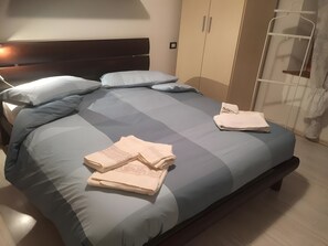 A neatly made bed with a blue and grey bedspread, two folded towels, and a wooden headboard. - Apartment 'Nina' with Shared Terrace and Wi-Fi (Santo Stefano di Cadore)