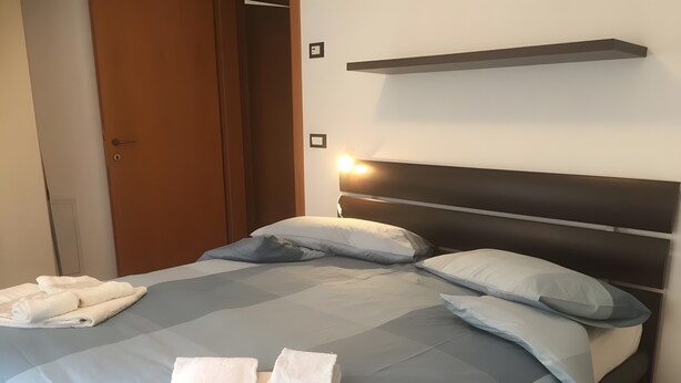 A neatly made bed with pillows and folded towels, a wooden door, and a wall-mounted shelf. - Apartment 'Nina' with Shared Terrace and Wi-Fi (Santo Stefano di Cadore)