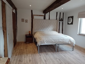 Ein Schlafzimmer mit Holzboden, einem Bett mit weißem Kopfteil, einem Nachttisch mit Lampe und einem Fenster mit Blick.