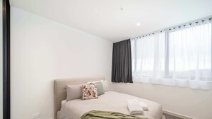 A hotel room with a bed, a window with curtains, a power outlet, and a green throw blanket. - Prestige 2BR Stay w/ Ocean Views, Rooftop & Cinema (Newcastle West)