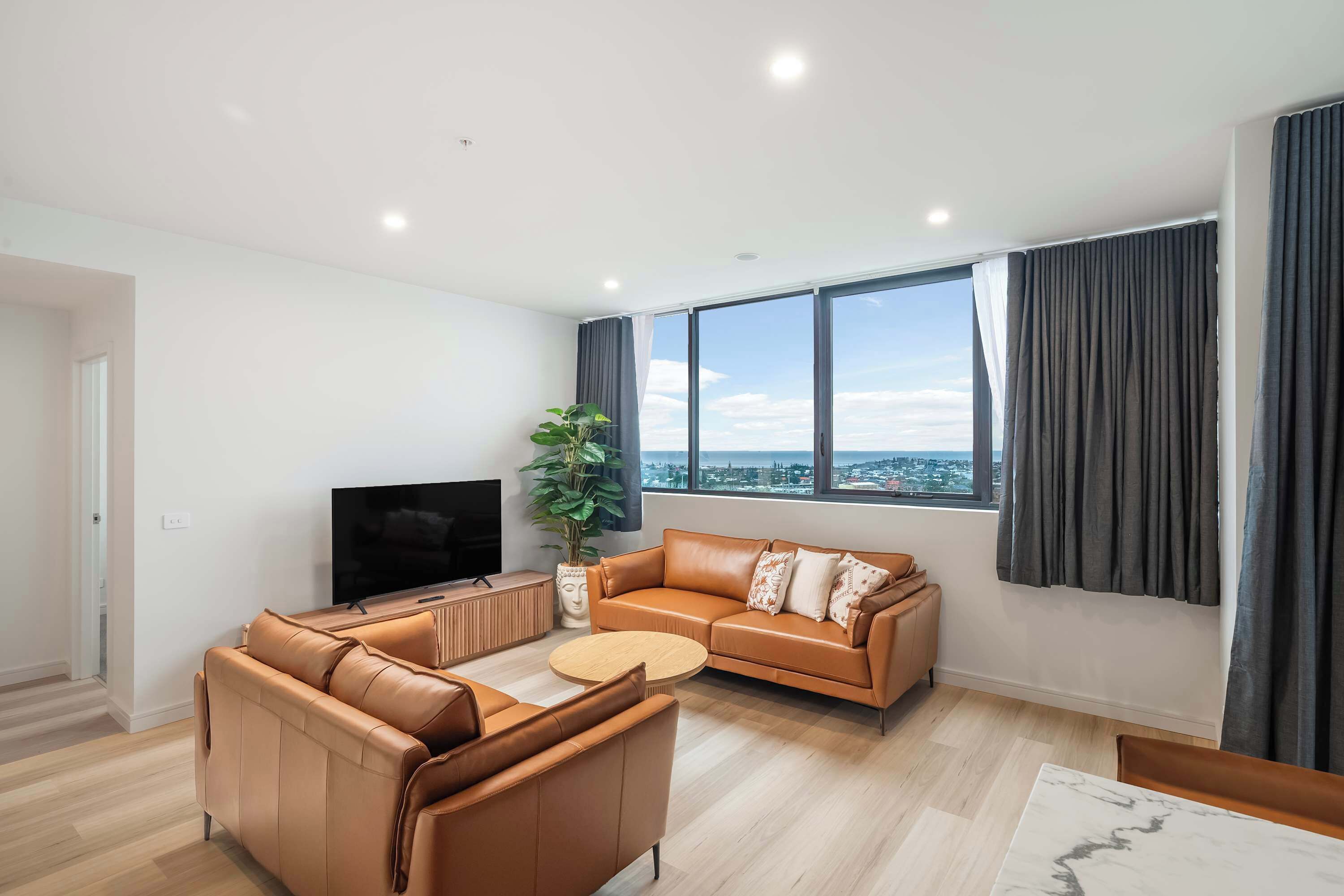 A modern living room with a sofa, TV, and a large window with curtains.