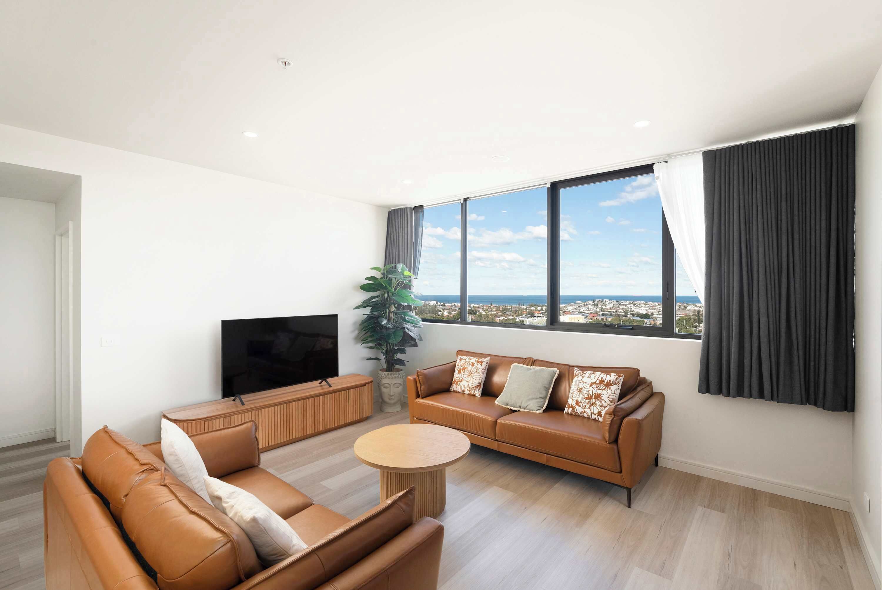 A modern living room with a sofa set, a coffee table, a TV, and a large window with a city view.