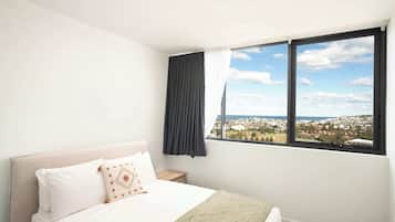 A bedroom with a bed, a nightstand, a window with a view of a town and sea, and a curtain.
