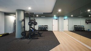 A gym with a squat rack, bench, and dumbbells. - Prestige 2BR Stay w/ Ocean Views, Rooftop & Cinema (Newcastle West)