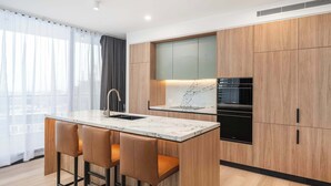 A modern kitchen with a marble island, bar stools, wooden cabinets, and a black dishwasher. - Prestige 2BR Stay w/ Ocean Views, Rooftop & Cinema (Newcastle West)