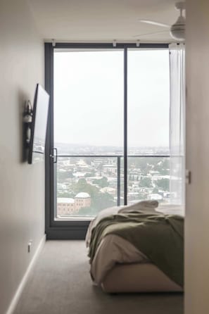 A bedroom with a large window, a bed, a ceiling fan, and a mounted TV. - Prestige 2BR Stay w/ Ocean Views, Rooftop & Cinema (Newcastle West)
