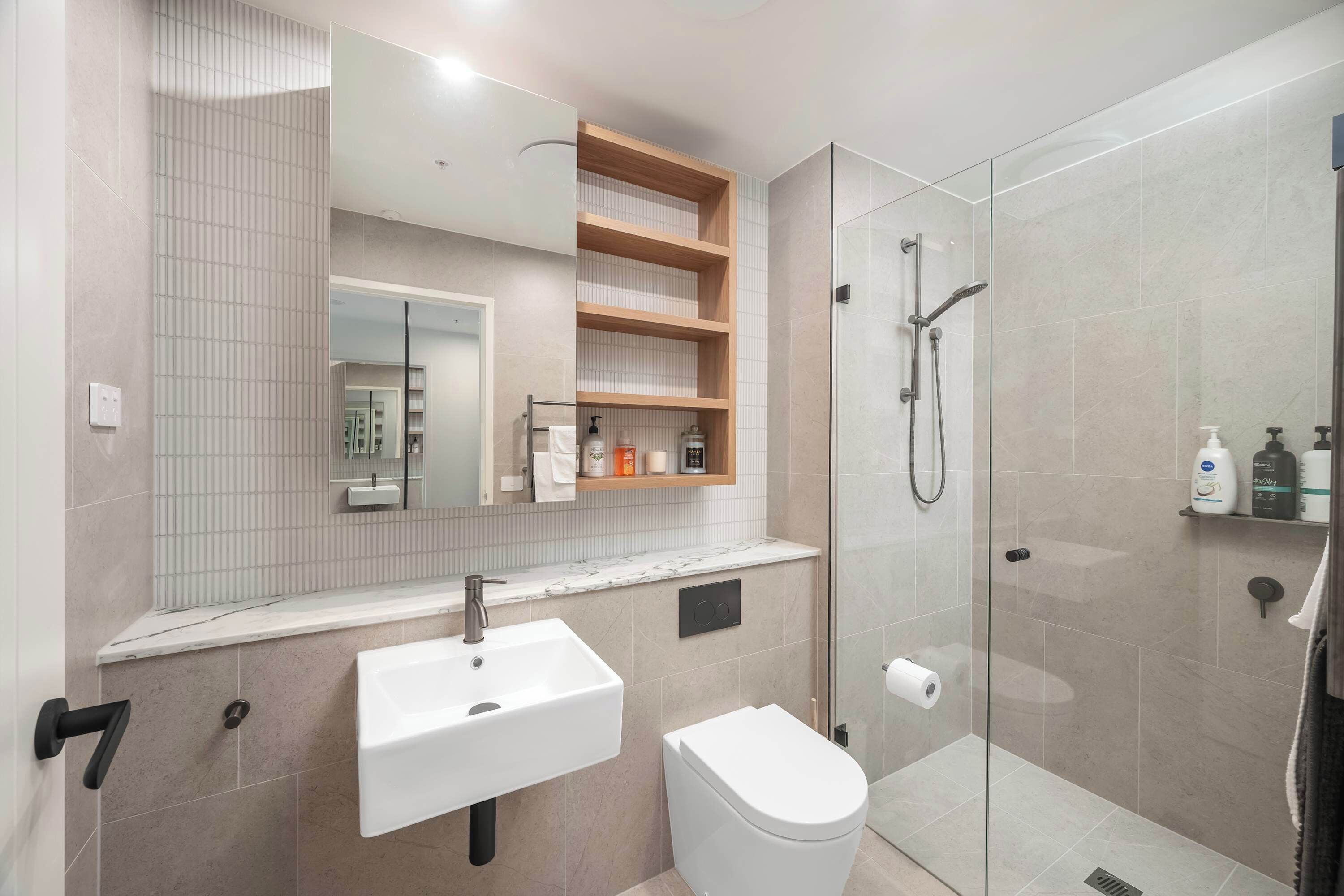A modern bathroom with a glass-enclosed shower, a white sink, and a toilet.