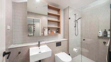 A modern bathroom with a glass-enclosed shower, a white sink, and a toilet.