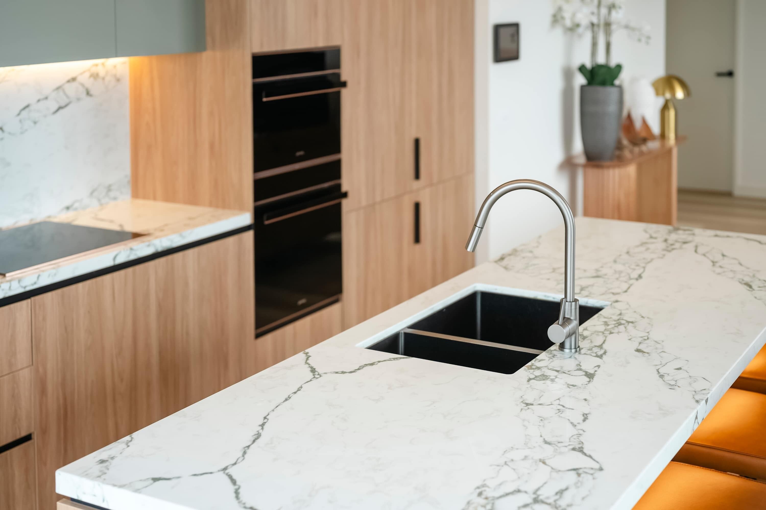 A kitchen with a marble countertop, a sink, wooden cabinets, and a built-in oven.