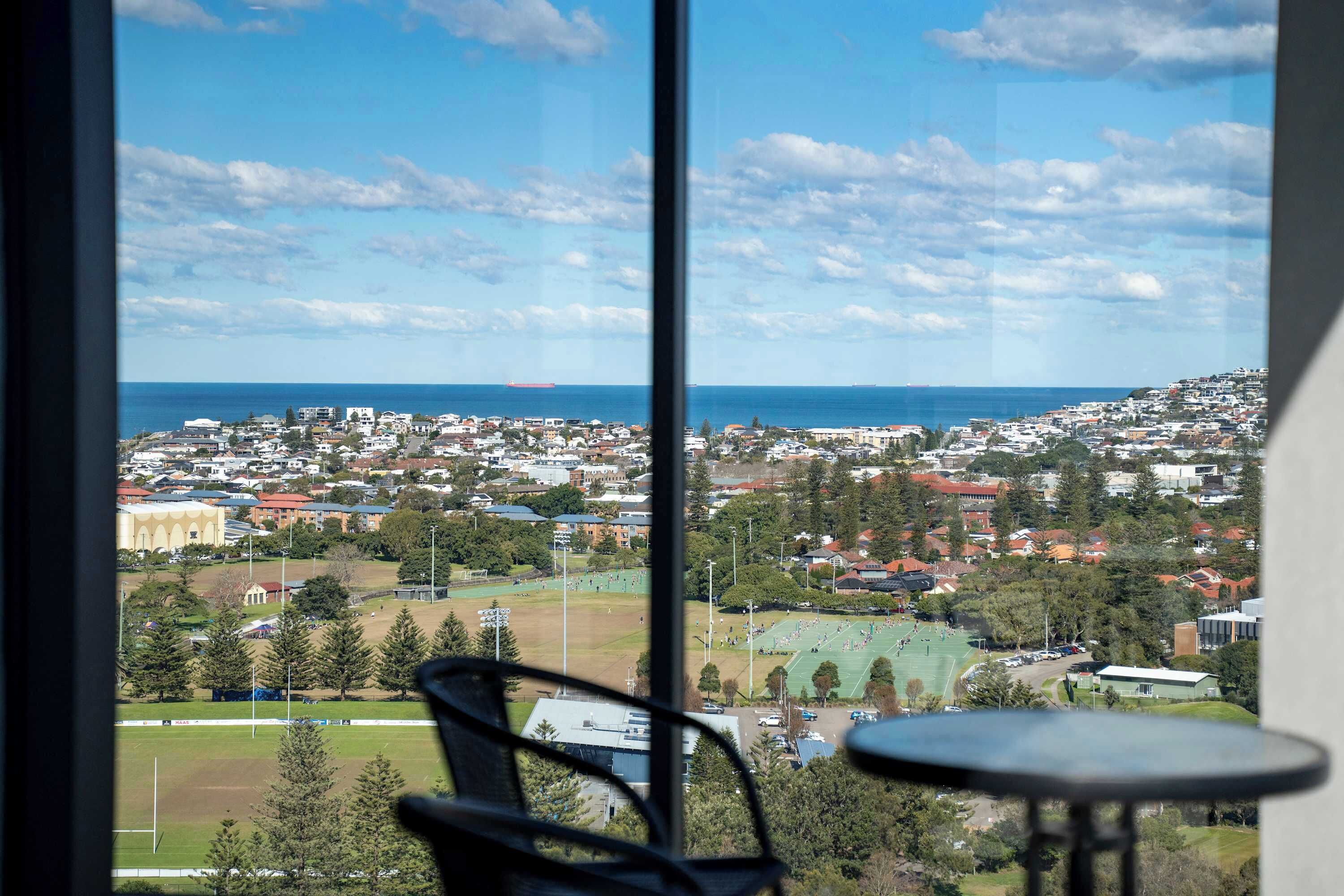 A view from a window overlooking a coastal town with a sports field and residential buildings.