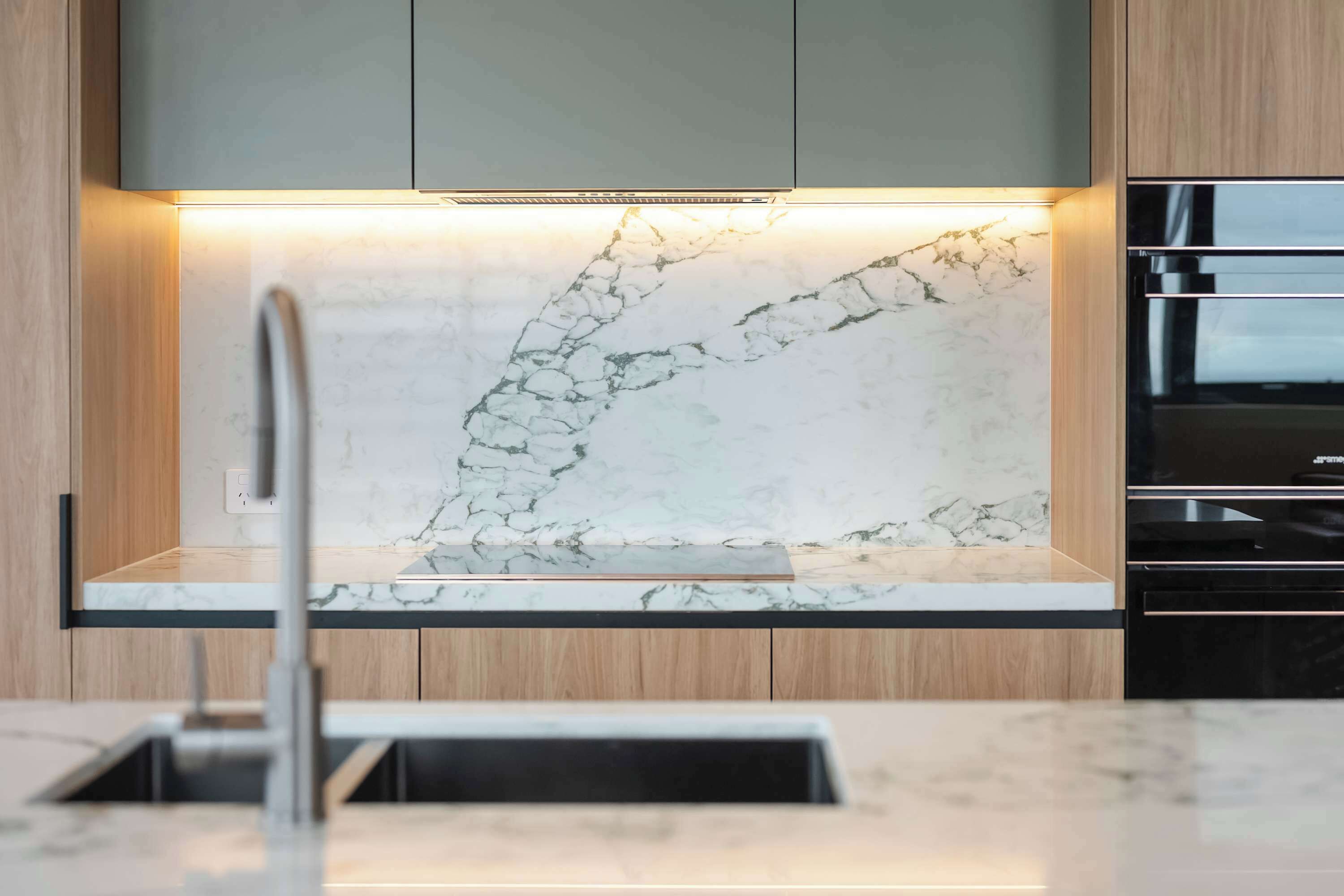 A kitchen with a marble backsplash, wooden cabinets, and a stainless steel oven.