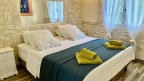 A bedroom with a stone wall, a bed with white bedding, a teal bedspread, and two yellow towels. - House 6 persons between vineyards and garrigues (Pouzilhac)