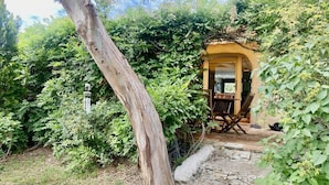 A rustic wooden structure with a stone pathway leading to a yellow door, surrounded by dense greenery. - House 6 persons between vineyards and garrigues (Pouzilhac)
