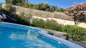 A swimming pool with a wooden deck, surrounded by lush greenery and a wooden fence. - House 6 persons between vineyards and garrigues (Pouzilhac)