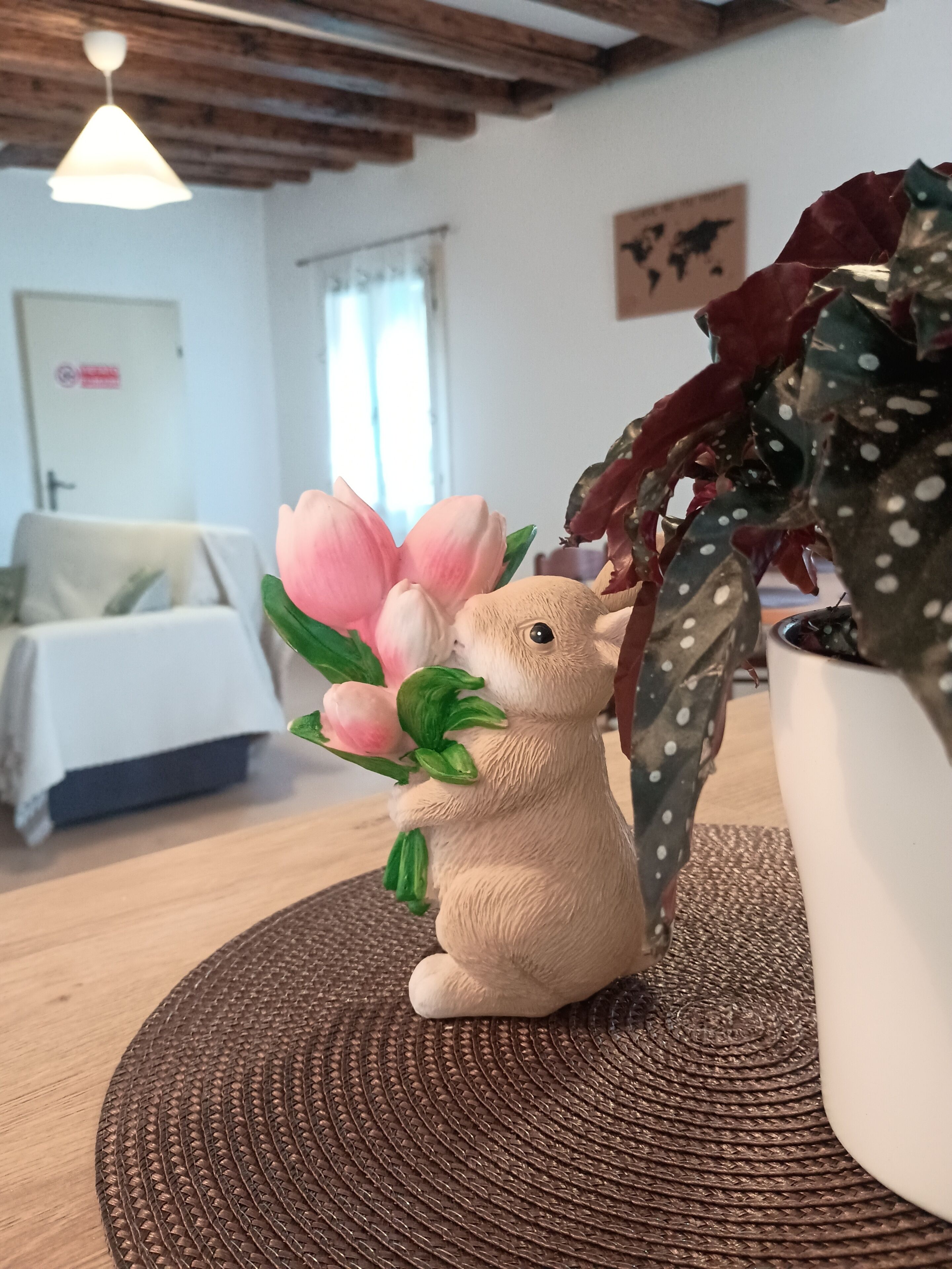 A small figurine holding a pink flower, a cactus, and a woven placemat on a table.