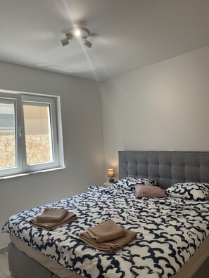 A bedroom with a bed, a window, a ceiling fan, and a bedside table with a lamp. - Apartment Mariner 2 With Heated Pool (Nin)