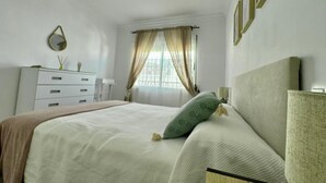 Un dormitorio con cama, cómoda, espejo y ventana con cortinas.