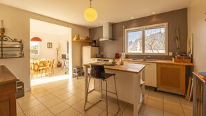 Une cuisine moderne dotée d’un îlot central, d’un coin repas avec une table et des chaises, et d’une grande fenêtre qui laisse entrer la lumière naturelle.