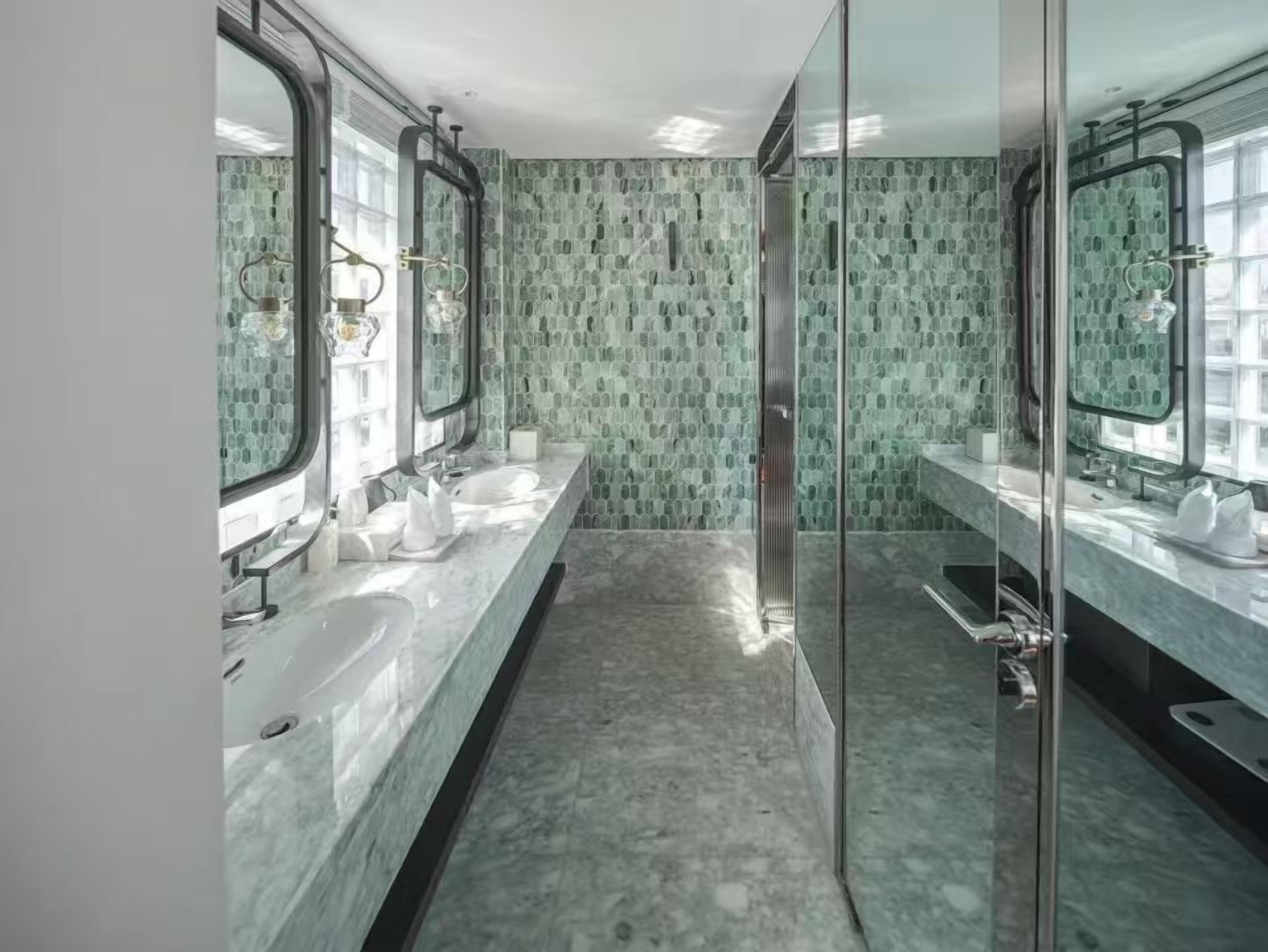 Un baño moderno con dos lavamanos, cabina de ducha de vidrio y un papel tapiz estampado.