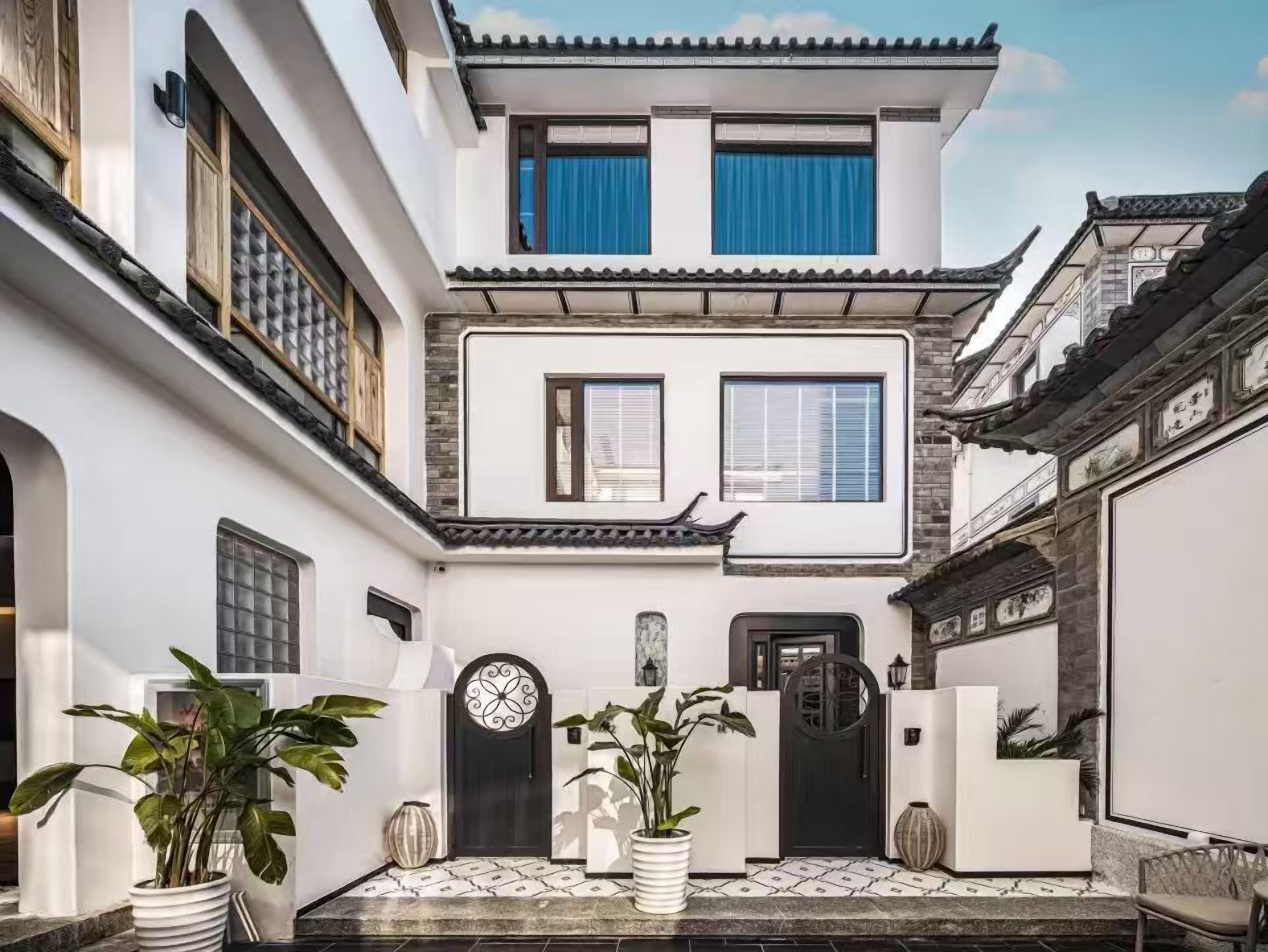 Edificio tradicional con un patio central, que presenta una puerta negra, dos ventanas con cortinas azules y plantas en macetas.