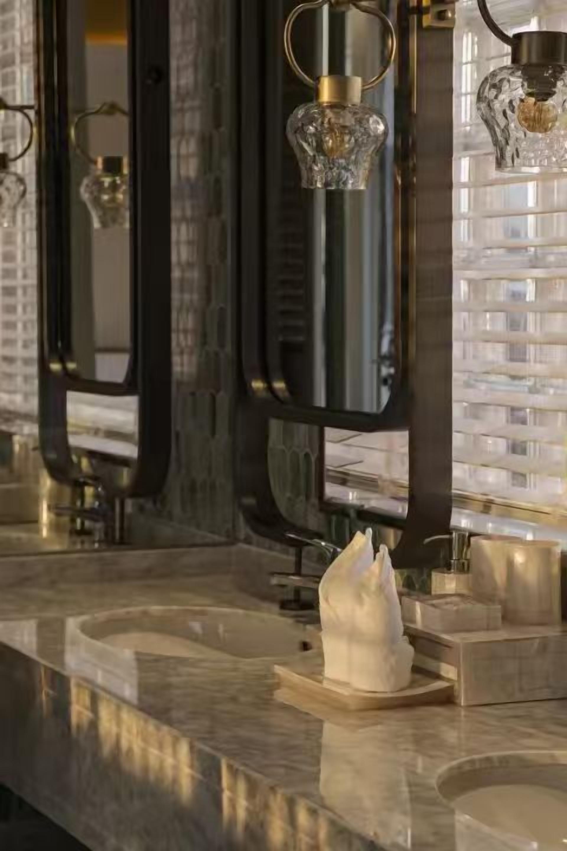 A modern bathroom with marble countertops, a white tissue dispenser, and a glass sculpture.