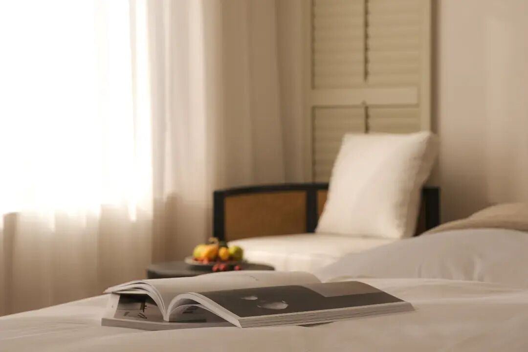 A hotel room with a bed, a bedside table with fruits, and a book on the bed.