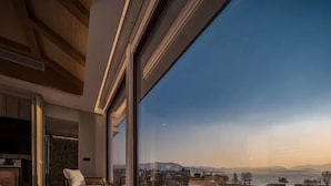 Ein modernes Zimmer mit großem Fenster, einem Bett, einem Sessel und einem kleinen Tisch.