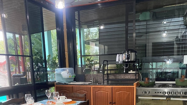 Un coin repas avec une table dressée pour quatre personnes, une cuisine équipée d’une cuisinière et d’un évier, et de grandes fenêtres offrant une vue sur la verdure.